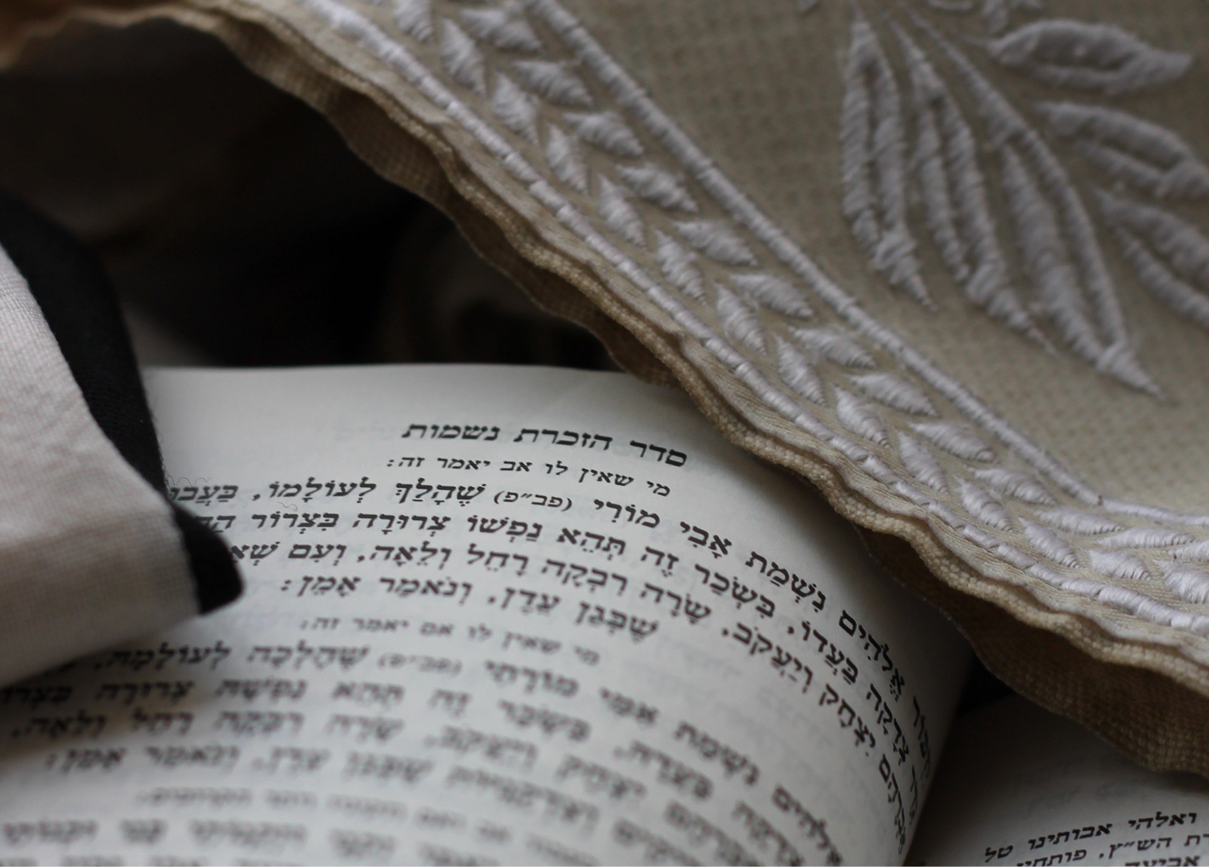 Um livro aberto com textos em hebraico e a borda de um talit cobrindo parte do livro