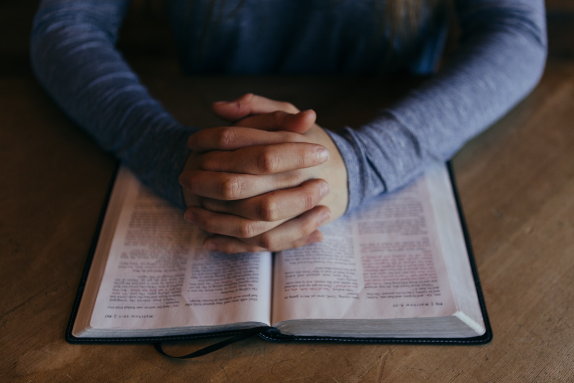 homem com as mãos entrelaçadas em cima de uma Bíblia